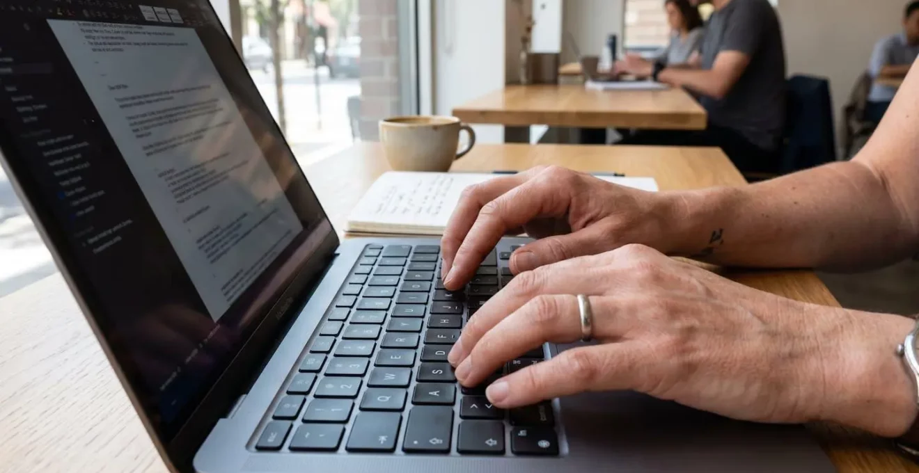 Primer plano extremo de manos de una persona de mediana edad tecleando en un teclado de ordenador portátil moderno con fondo completamente difuminado en bokeh
