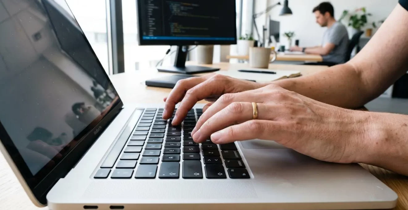 Primer plano extremo de manos de una persona de mediana edad tecleando en un teclado de ordenador portátil moderno con fondo completamente difuminado en bokeh