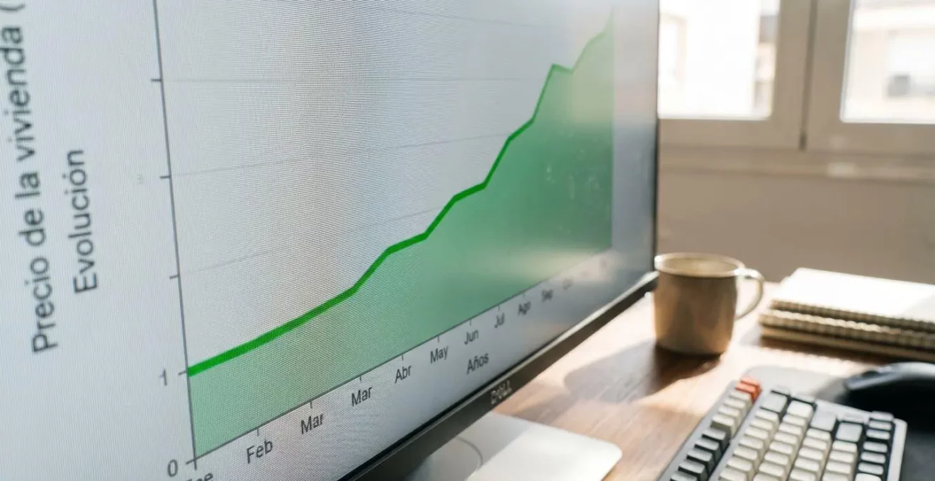 Pantalla de ordenador mostrando gráficos de evolución de precios inmobiliarios con líneas de tendencia ascendente sobre fondo de oficina